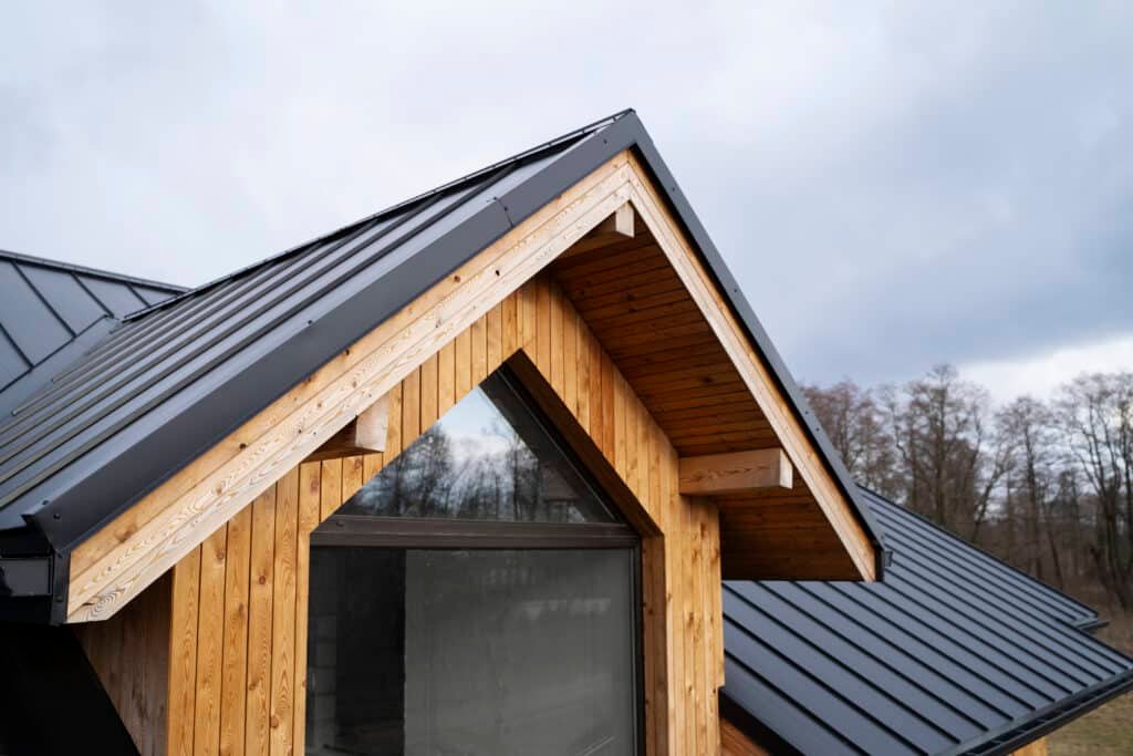 Coin d'une maison en bois avec toit en métal et ciel nuageux.