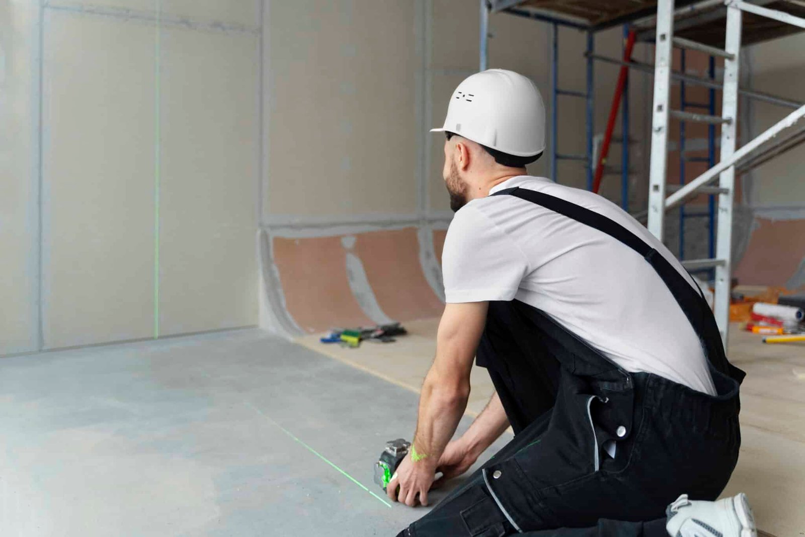 Ouvrier mesurant le sol avec un laser dans un intérieur en rénovation.