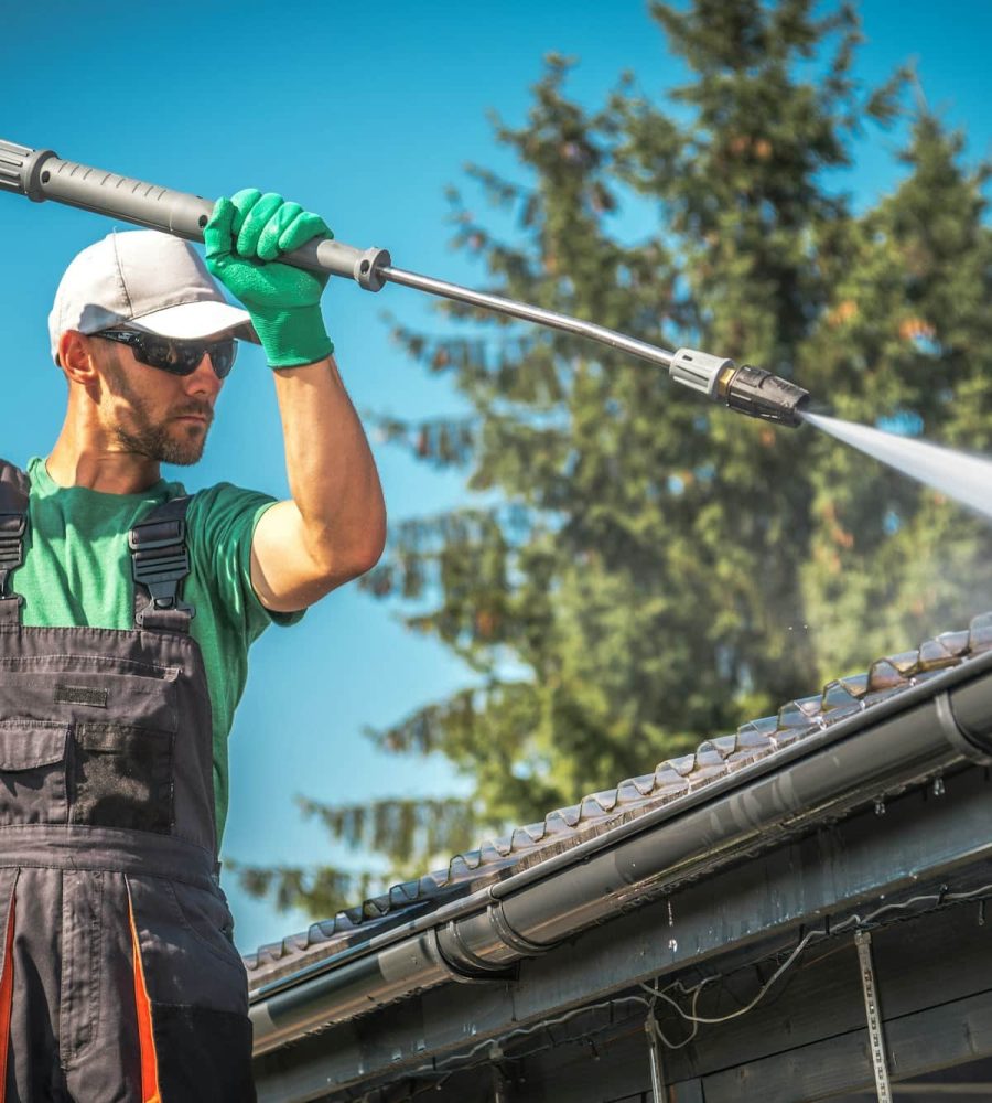 Ouvrier utilisant un nettoyeur haute pression pour nettoyer un toit de carport.